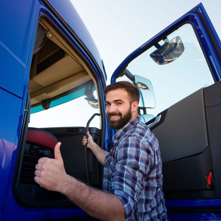 Professional truck driver entering his truck long vehicle and holding thumbs up. Loving his job. Transportation services.